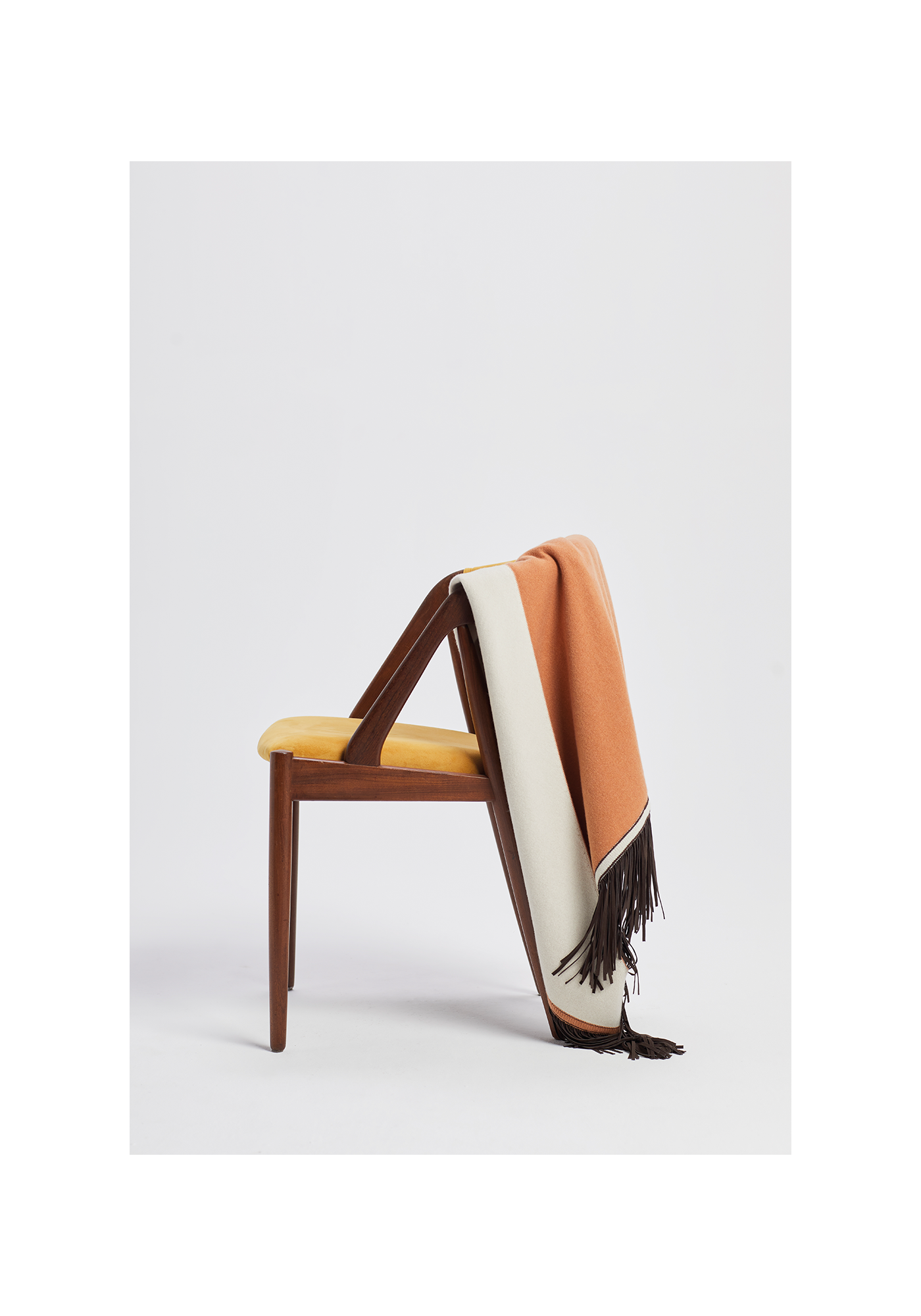Antonia Zander Triangolo cashmere scarf with leather fringes draped over a wooden chair.